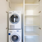 Front view of washing machine and dryer in a white cabinet with open doors. Nobody inside